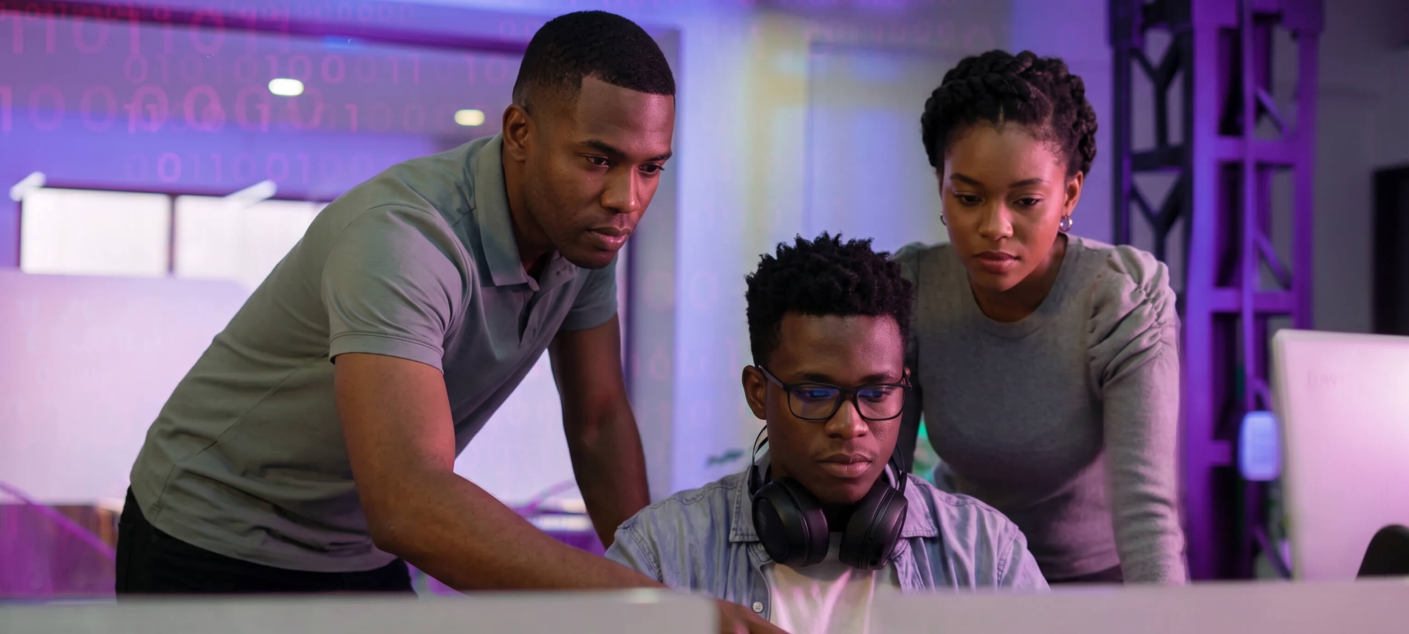 Three Black colleagues reviewing work together on a computer in a modern office.